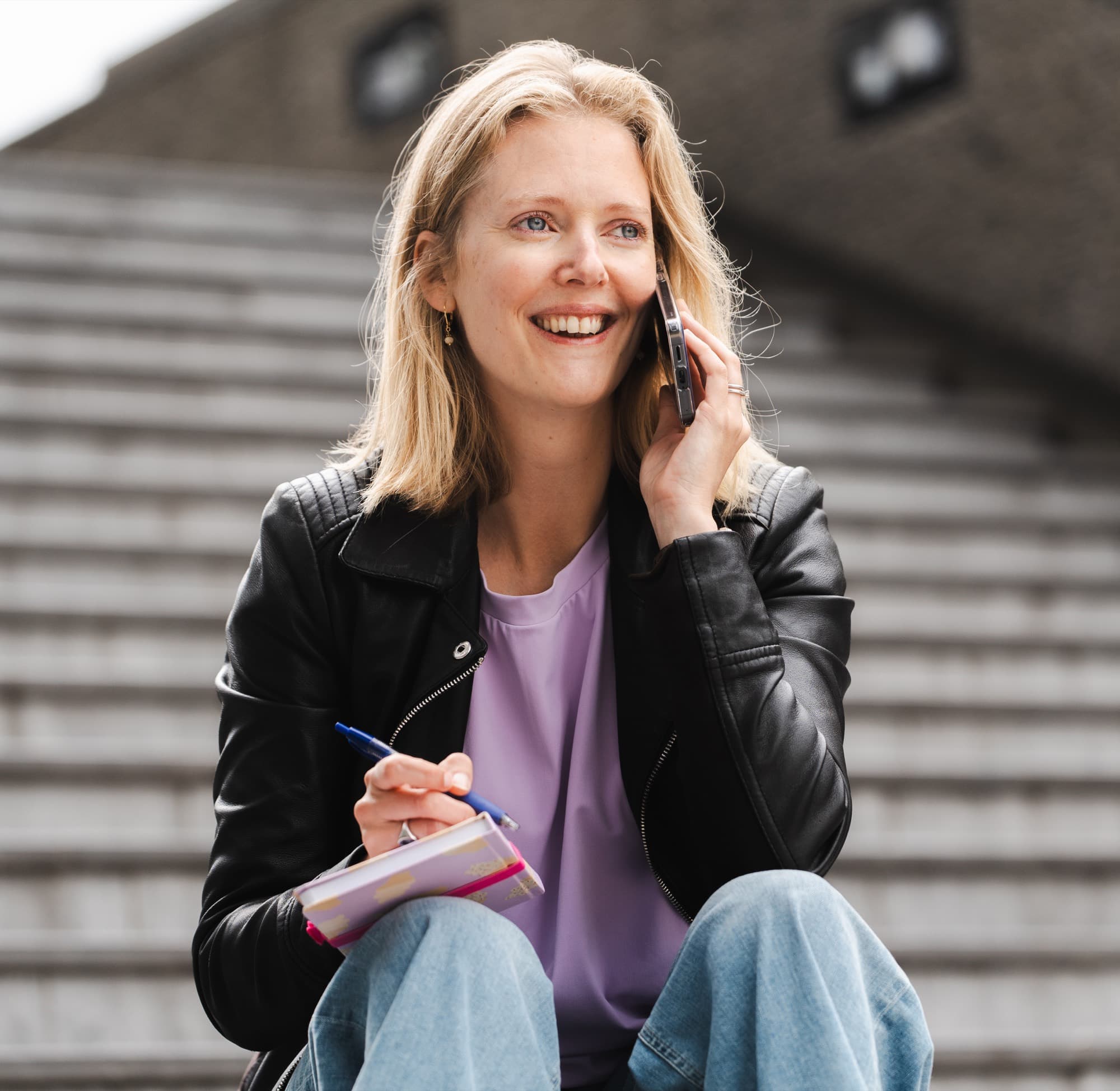 Lachende onderneemster aan de telefoon met notitieboek op een trap