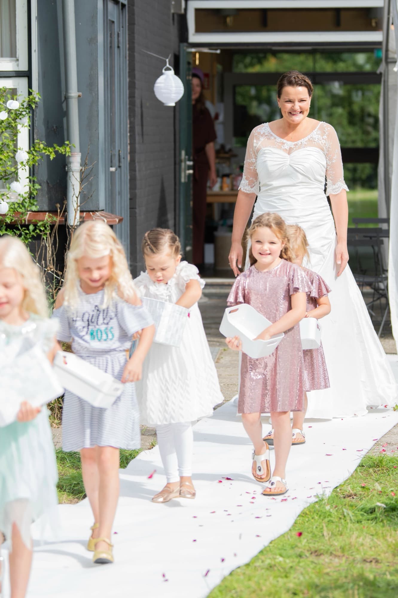 Bruid loopt met strooikinderen over de witte loper naar buiten