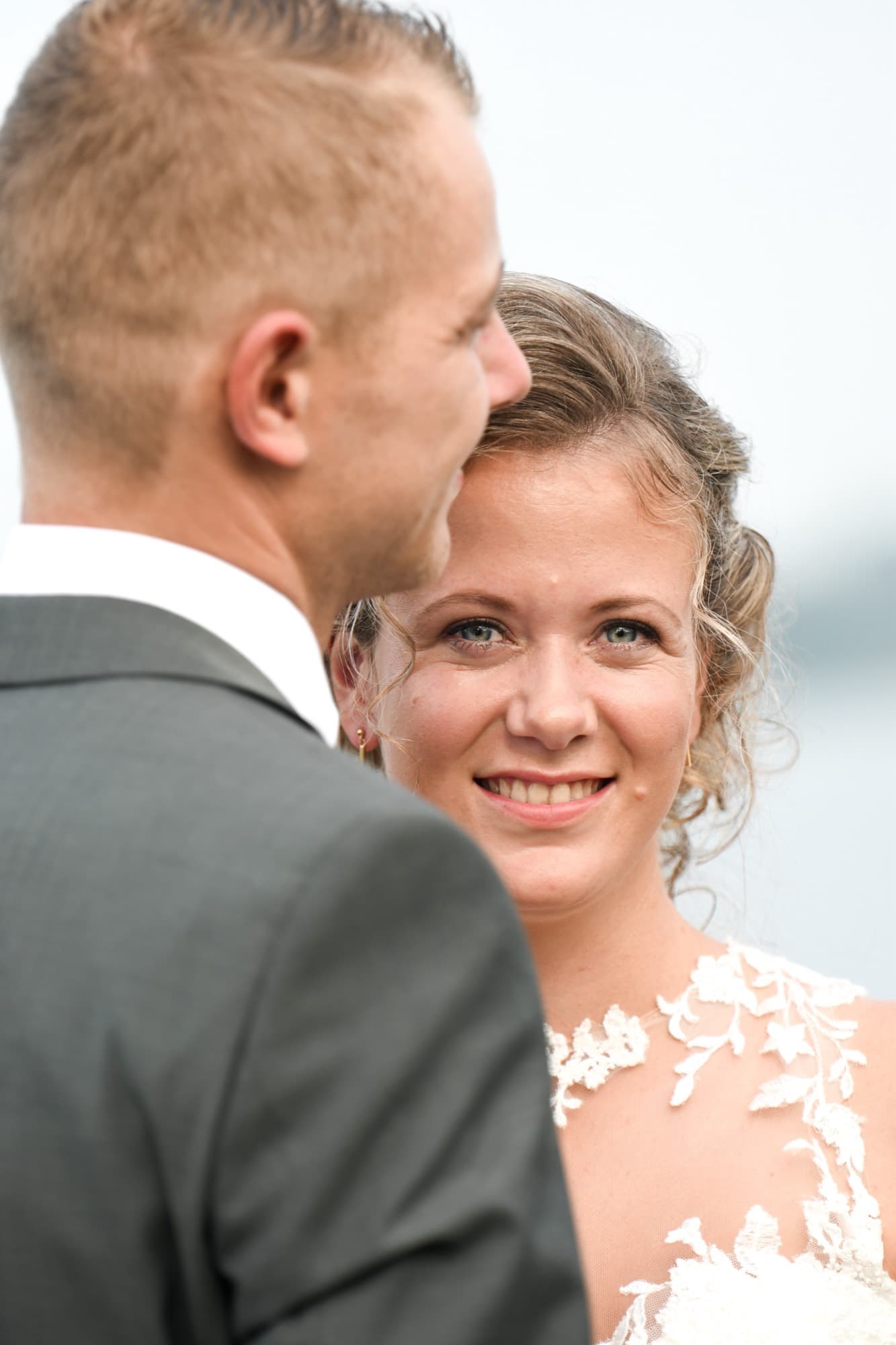 Bruid kijkt glimlachend over de schouder van haar bruidegom