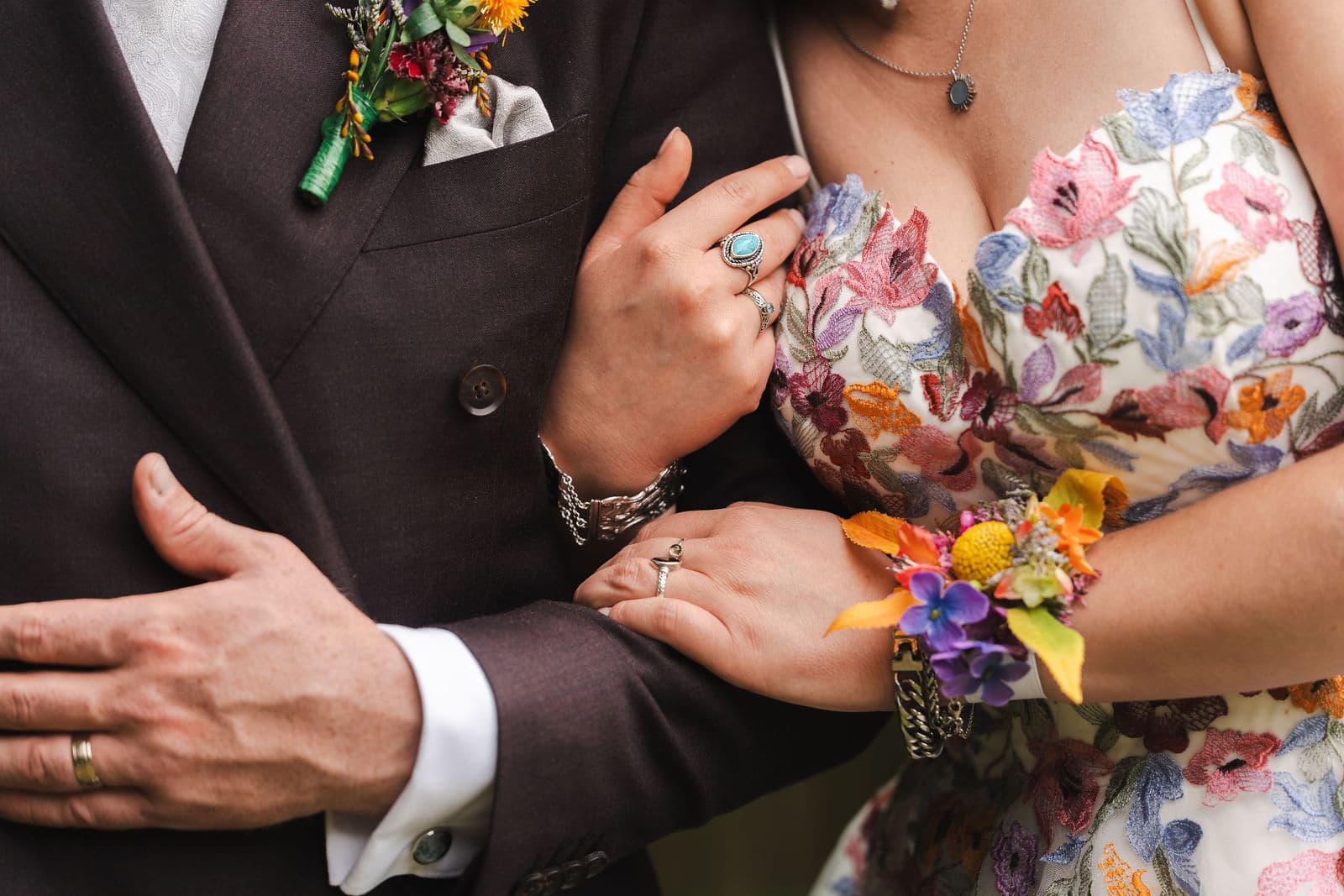 Detail van een bruidspaar met kleurrijke corsages en een gebloemde jurk