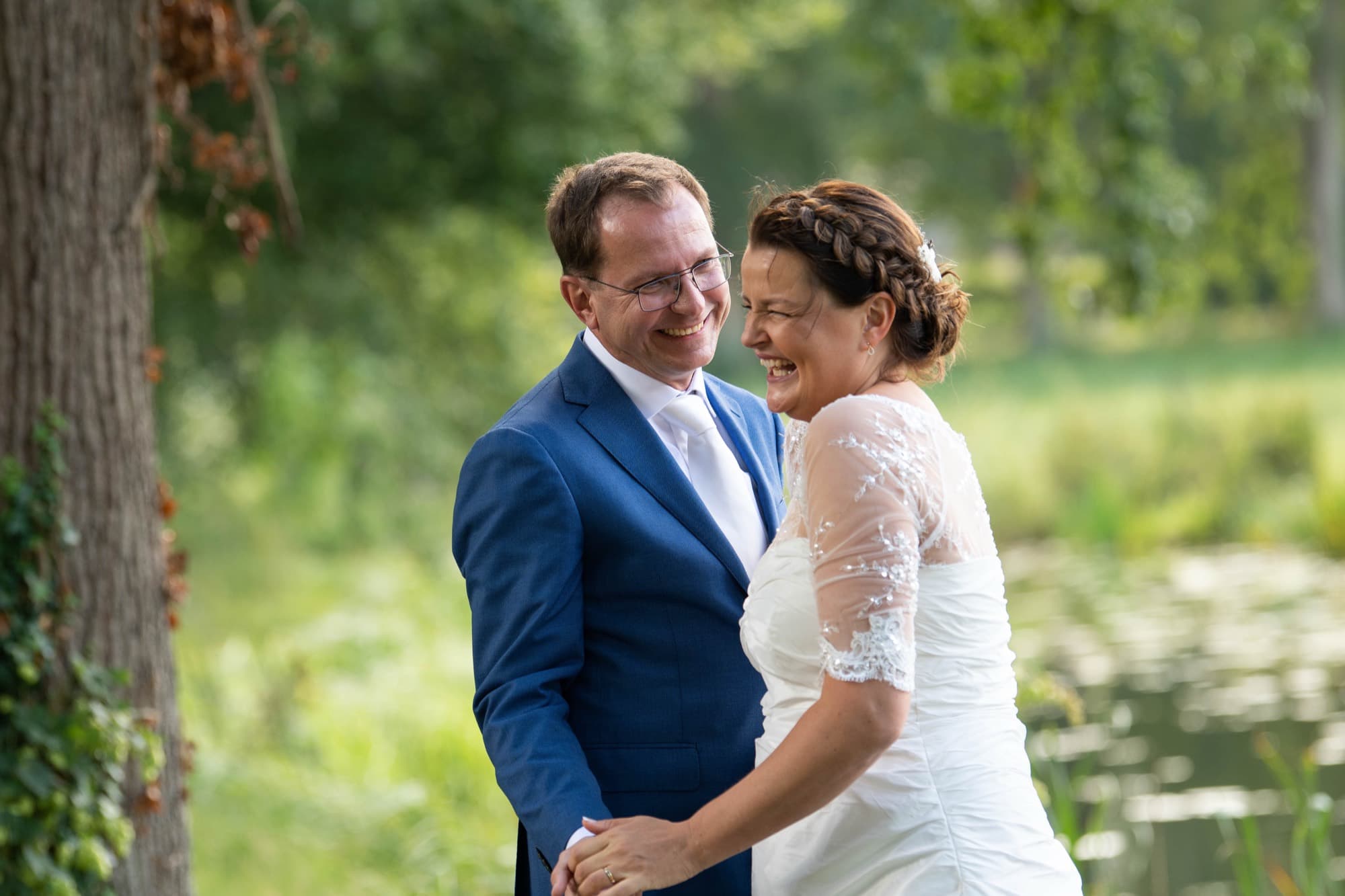 Lachend bruidspaar dicht bij elkaar aan de waterkant