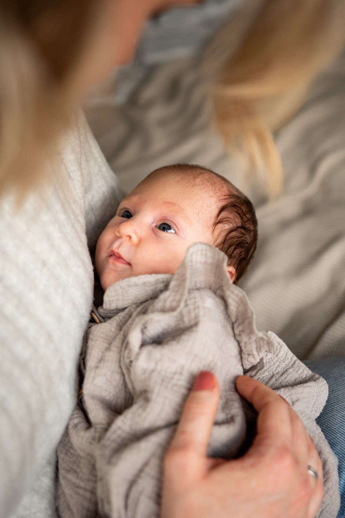 Pasgeboren baby kijkt omhoog vanuit de armen van moeder