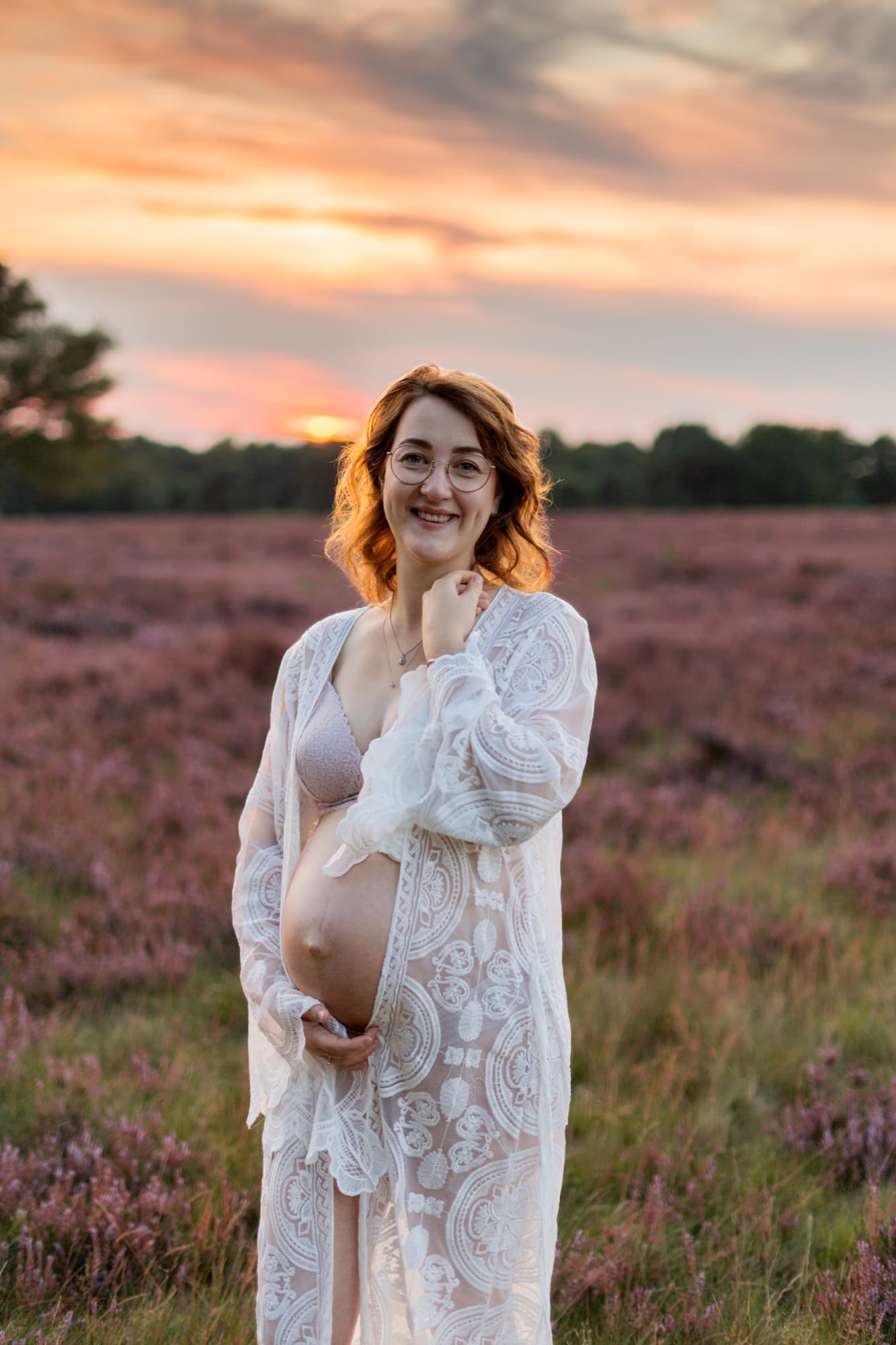Aanstaande moeder in een kanten jurk in de bloeiende heide bij zonsondergang